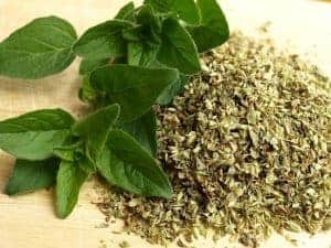 Frische Oregano-Bl&auml;tter neben getrockneten Oregano-Fl&ouml;ckchen auf Holzuntergrund