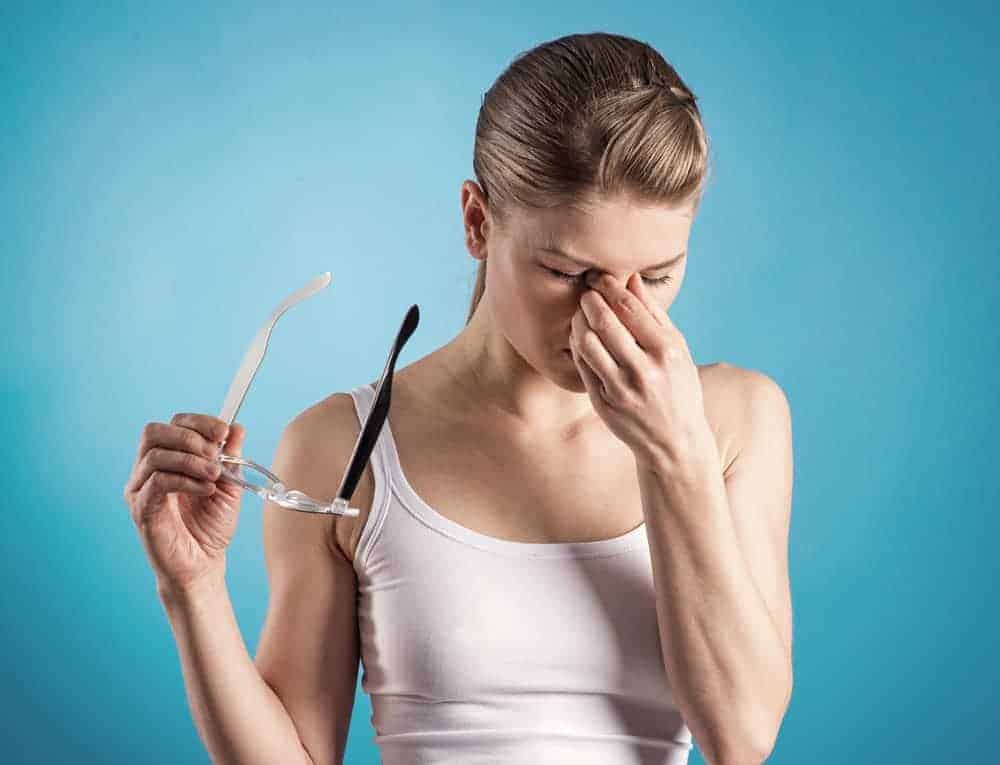 Junge Frau mit Brille und Kreislaufbeschwerden vor blauer Wand