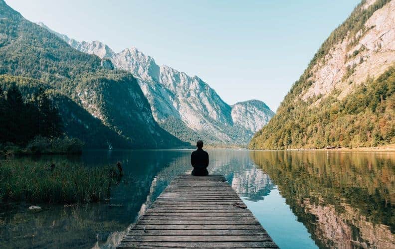 Mann, der auf Steg mit Blick auf See und Berge sitzt