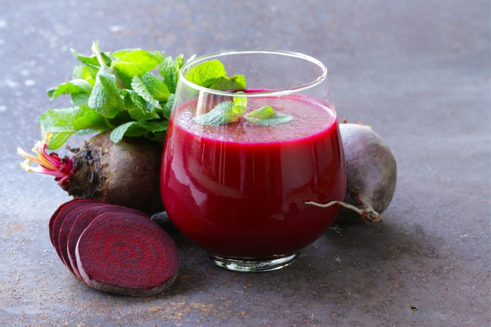 Rote Beete Saft in einem Glas, daneben liegen Scheiben einer Knolle