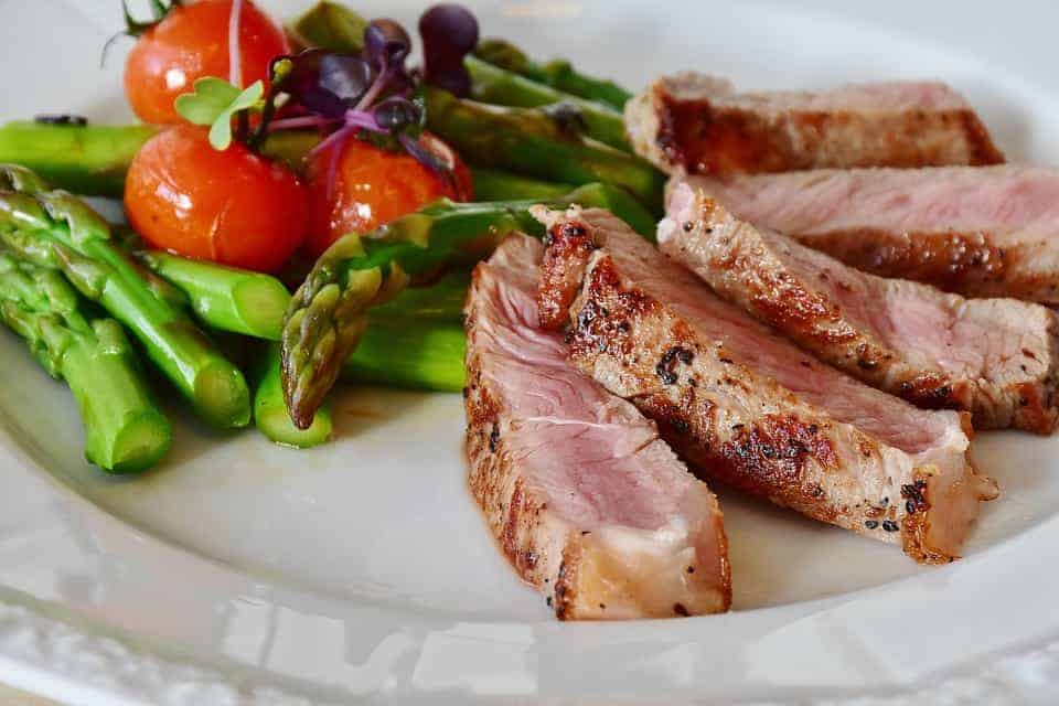 Kalbssteak-Scheiben mit gr&uuml;nem Spargel und Tomaten auf wei&szlig;em Teller