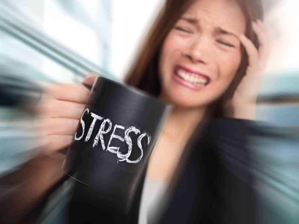 Junge Frau mit zusammengebissenen Z&auml;hnen und schwarzer Tasse mit Aufschrift "Stress"