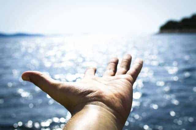 In Sonne gestreckte Hand mit Meer im Hintergrund