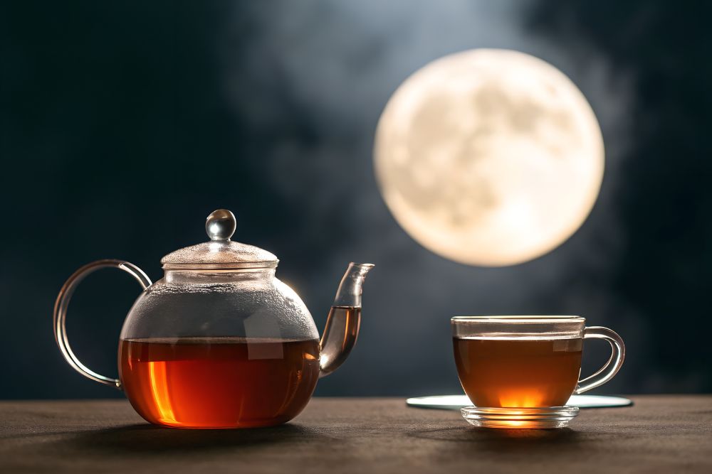 Eine gl&auml;serne Teekanne und eine Glastasse mit Tee auf einem Tisch, im Hintergrund scheint der Vollmond