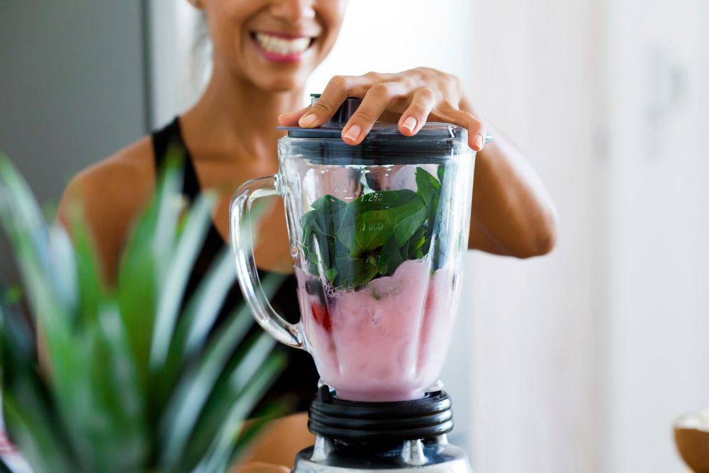 Frau macht Smoothie mit Mixer