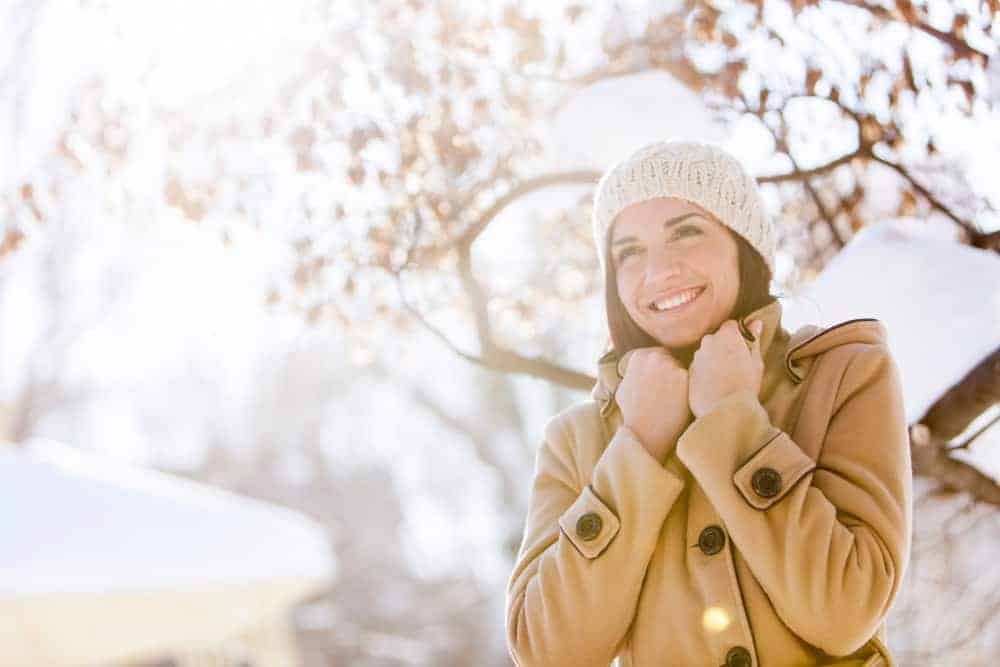 Frau in einem Wintermantel steht vor einem fast vollst&auml;ndig entlaubten Baum