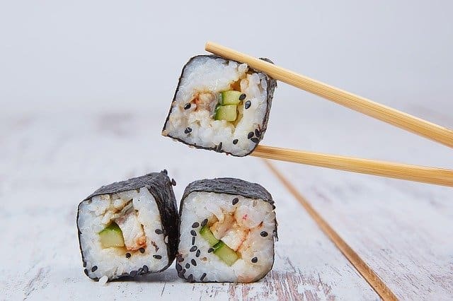 Drei fertige Sushi mit Stäbchen auf Holztisch