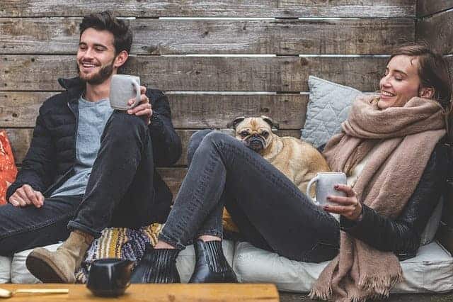 Zwei Freunde machen Kaffepause mit Mops im Hintergrund