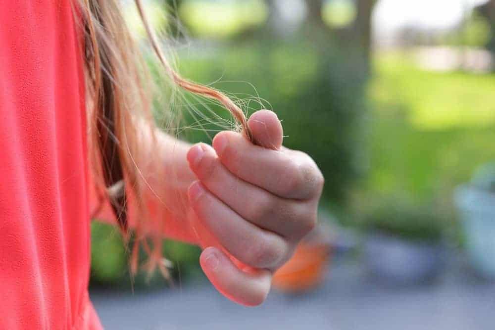 Frau zwirbelt eine blonde Haarsträhne
