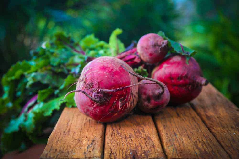 Vier frische Knollen rote Beete auf einem Holztisch