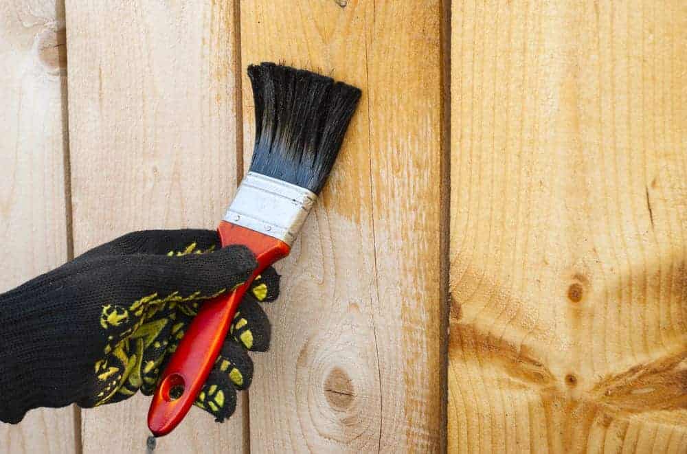 Lein&ouml;l wird mit gro&szlig;en Pinsel als Holzschutz auf helle Bretter aufgetragen