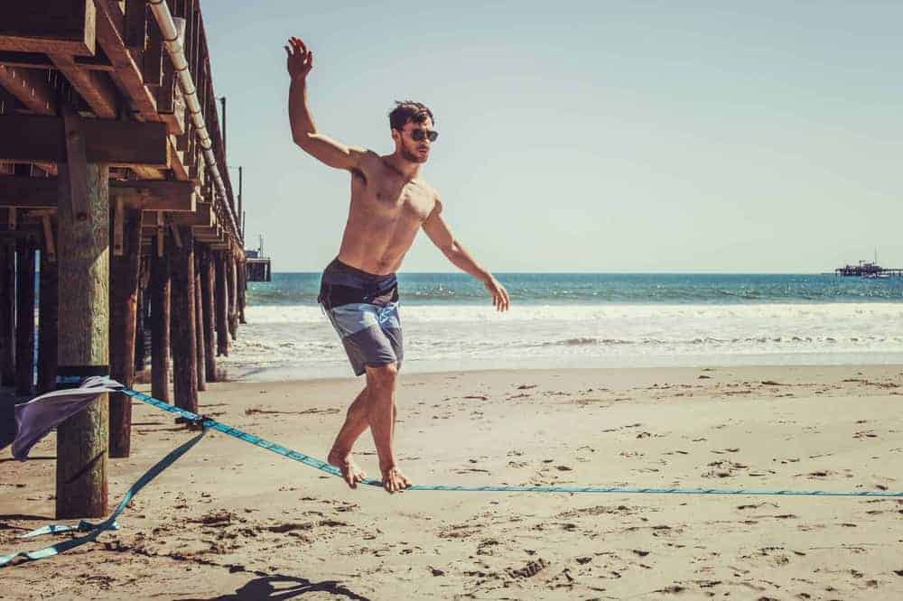Junger Mann auf Slackline am Strand mit Meer im Hintergrund