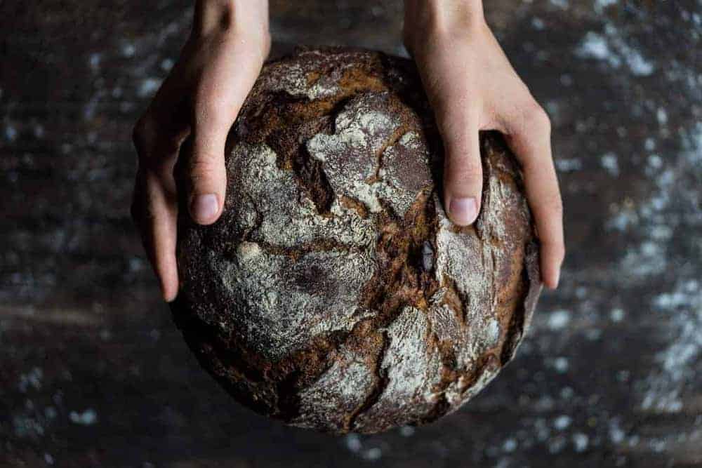 Knuspriges, dunkelbraunes Brot umfasst von zwei H&auml;nden in Nahaufnahme