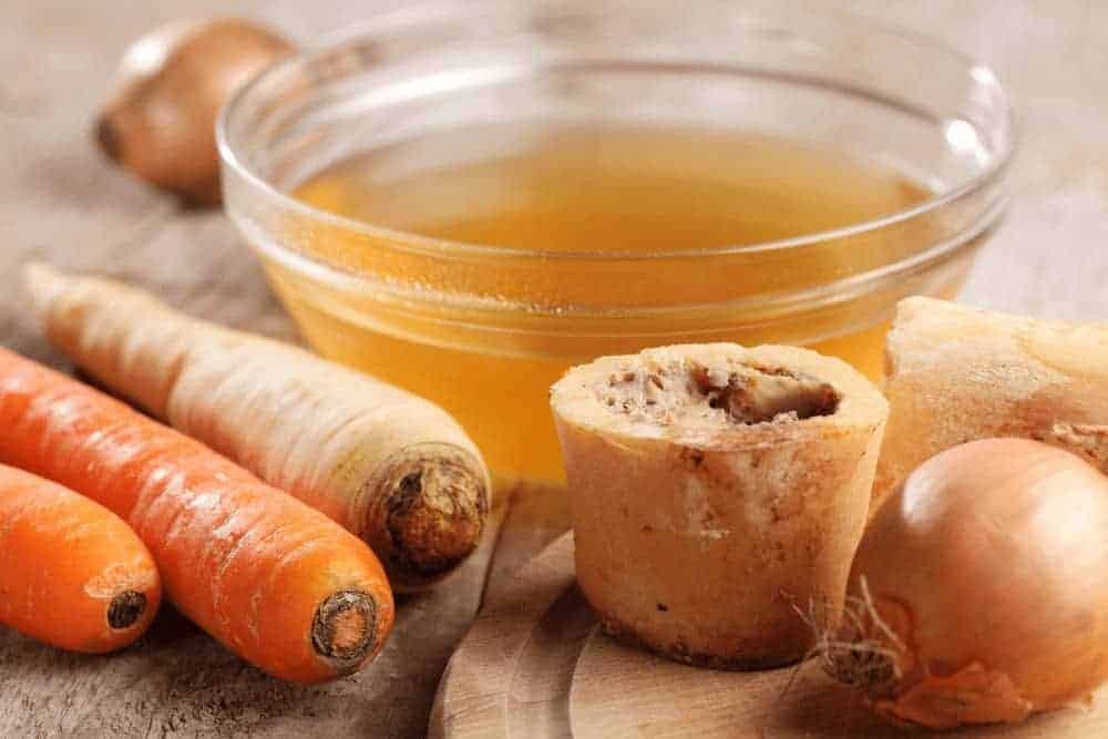 Knochenbr&uuml;he mit Karotten, Knochen und Zwiebeln auf einem Tisch