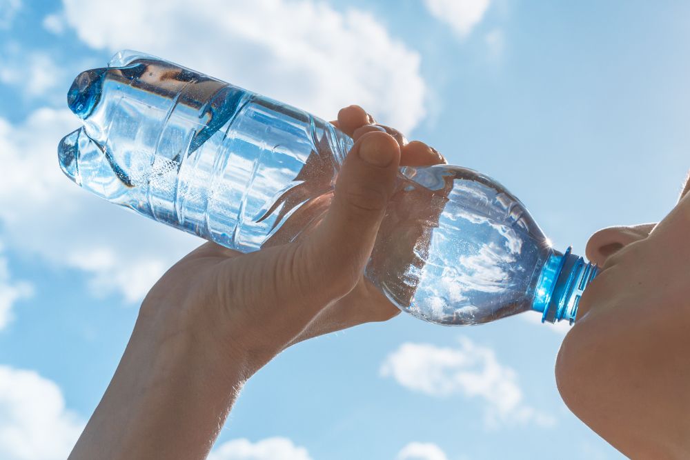 Person trinkt aus einer Wasserflasche vor blauem Himmel