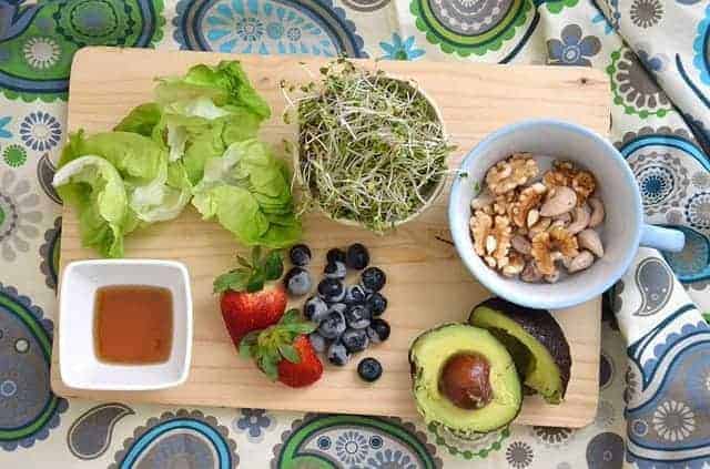 Brokkolisprossen mit Beeren, Nüssen und Avocados auf Holzbrett arrangiert