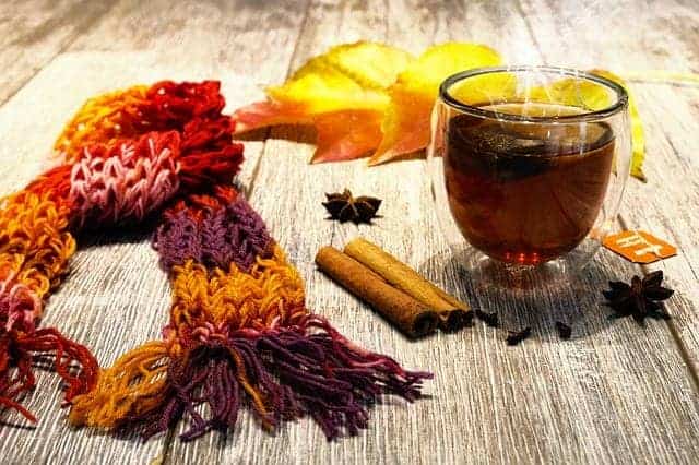 Hei&szlig;er Zimttee mit Zimstangen, buntem Schal und Herbstlaub auf Holztisch