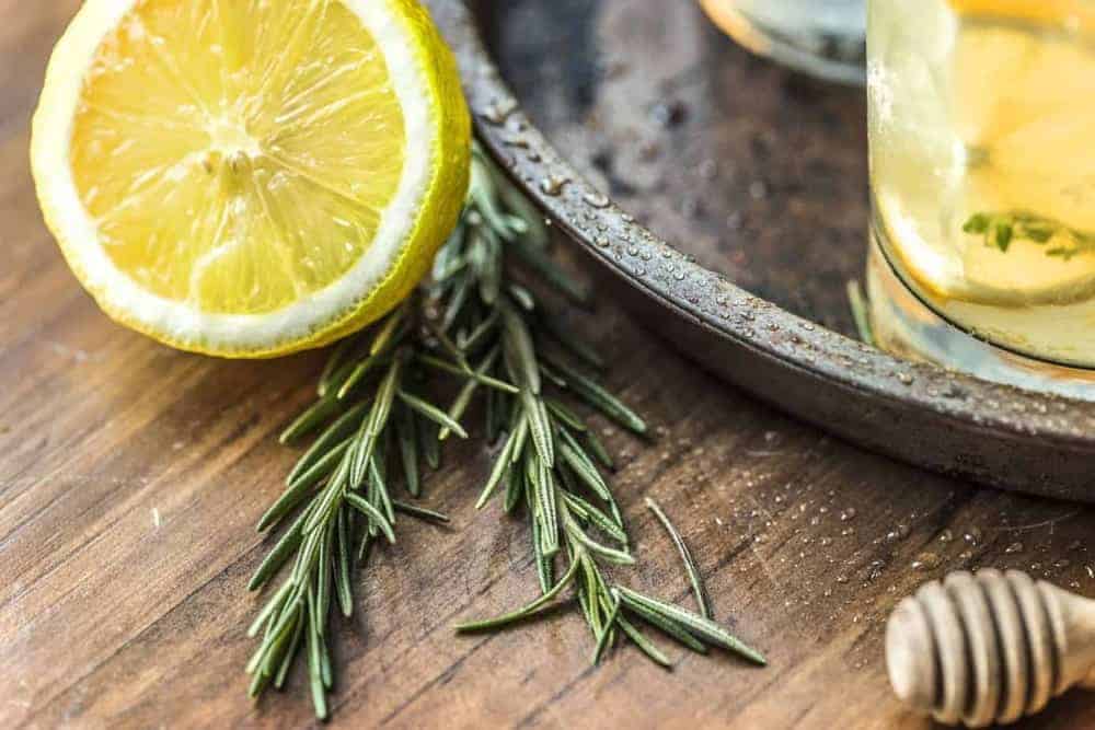 Aufgeschnittene Zitrone mit Rosmarin-Zweig und Honigdripper auf Holztisch