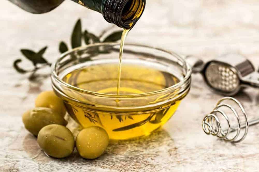Oliven&ouml;l in Glas-Sch&auml;lchen neben gr&uuml;nen Oliven und Olivenzweig