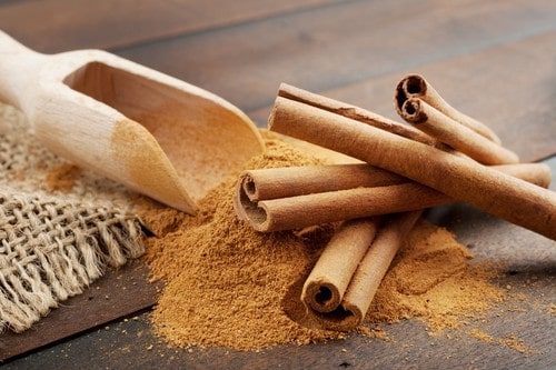 Zimt Pulver und Zimtstangen auf dunkler Holzplatte, Holzl&ouml;ffel und S&auml;ckchen