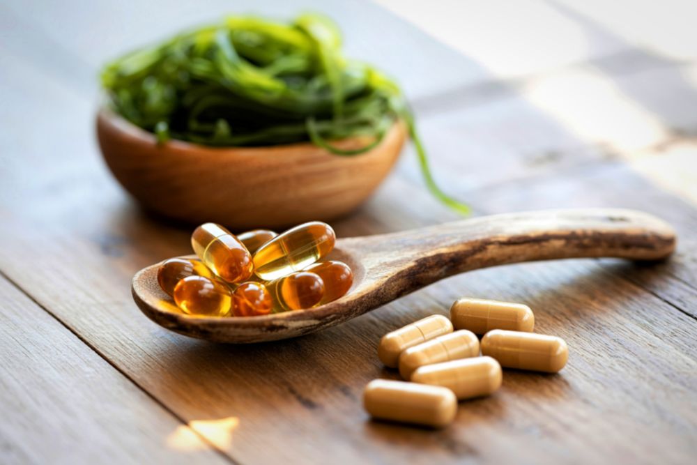 Omega-3-Kapseln und eine Holzschale mit Algen auf einem Tisch