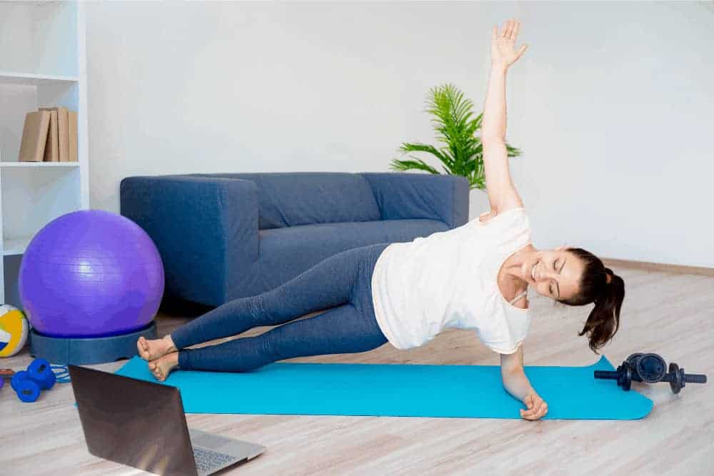 Frau macht Seitbeuge auf Sportmatte vor ihrer Couch im Wohnzimmer
