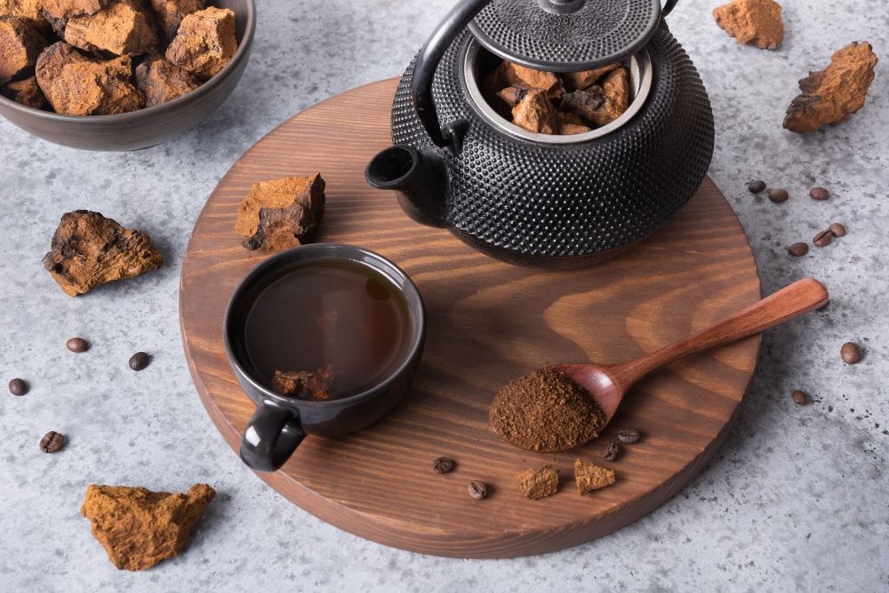 Chaga-Tee in einer Tasse und in einer Kanne, daneben Chaga-Brocken