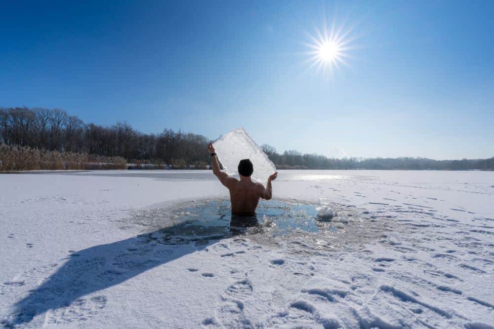 Mann steht in einem vereisten See und h&auml;lt eine Eisscholle hoch